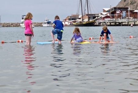 Kids with body boards at Dana Point and the now-demised Ocean Institute Pilgrim tall ship in the background